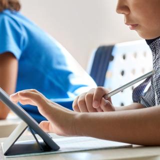 Close up cut shot of elementary student using tablet device sitting in classroom